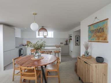 A kitchen and dining area with a round wooden table and chairs a wooden sideboard and wall art at Ysgol Fach Little School in Benllech