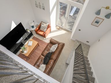 A living room with a brown leather sofa an armchair a coffee table and a large TV next to glass doors at Ysgol Fach Little School in Benllech