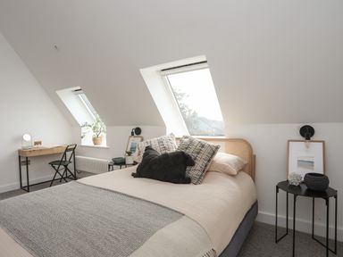 A bedroom with a bed pillows and side tables under sloping ceiling windows at Ysgol Fach Little School in Benllech