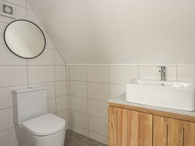 A bathroom with a toilet a round mirror and a sink on a wooden cabinet at Ysgol Fach Little School in Benllech