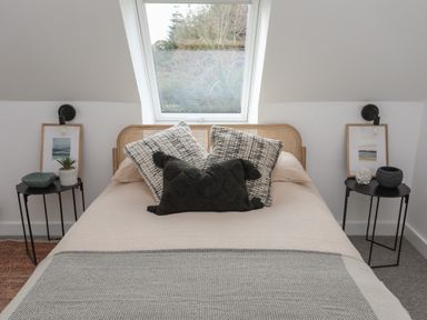 A bedroom with a bed under a skylight window with pillows and side tables with decor at Ysgol Fach Little School in Benllech