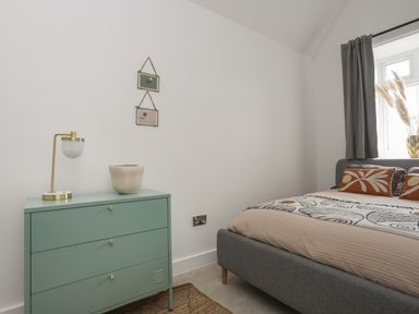A bedroom with a gray bed, green chest of drawers, lamp, and two framed pictures on the wall at Ysgol Fach Little School in Benllech