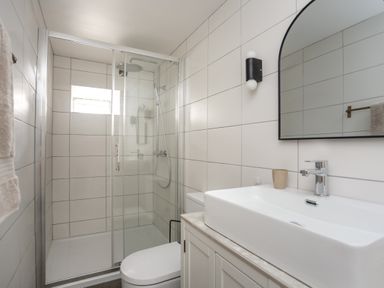 A bathroom with a glass shower enclosure toilet and sink with mirror at Ysgol Fach Little School in Benllech