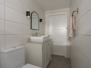 A bathroom with a toilet, vanity with sink, mirror, towel on a rack and white tiled walls at Ysgol Fach Little School in Benllech