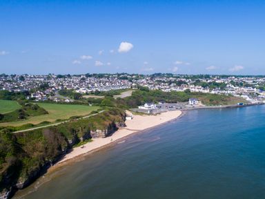 A coastal area with a beach cliffs green fields and houses in the background at Ysgol Fach Little School in Benllech