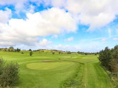 A golf course with putting greens and flags under a blue sky with clouds at Ysgol Fach Little School in Benllech