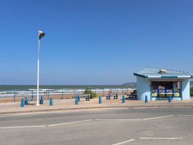 A beachside ice cream kiosk with benches and a flagpole near the sea at Ysgol Fach Little School in Benllech