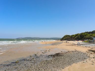 A beach with sand and pebbles and people walking by the water at Ysgol Fach Little School in Benllech