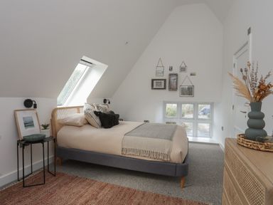 A bedroom with a bed under a skylight window a small table with framed picture and plants and a dresser with dried flowers at Ysgol Fach Little School in Benllech