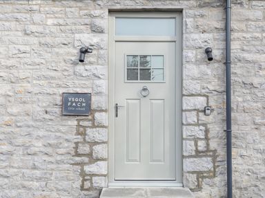 A grey door with window panes and a knocker on a stone wall with a sign reading Ysgol Fach little school at Ysgol Fach Little School in Benllech