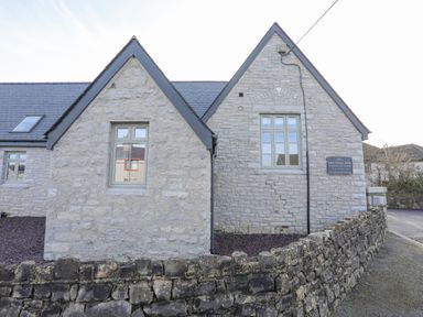 A stone building with two peaked roofs and windows behind a stone wall at Ysgol Fach Little School in Benllech