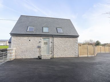 A stone house with a dark roof and three skylights a central door and a wooden fence at Ysgol Fach Little School in Benllech