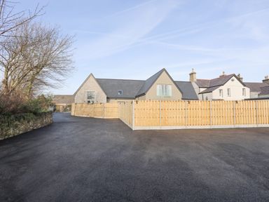 A paved driveway leading to houses with a wooden fence and leafless trees at Ysgol Fach Little School in Benllech