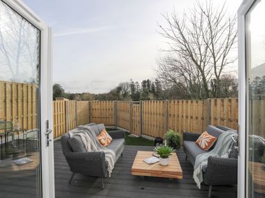 An outdoor patio with two gray sofas, a wooden coffee table, and a wooden fence at Ysgol Fach (Little School) in Benllech