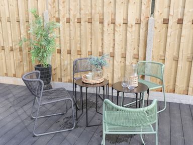 An outdoor seating area with four chairs around two small tables and a potted plant against a wooden fence at Ysgol Fach Little School in Benllech