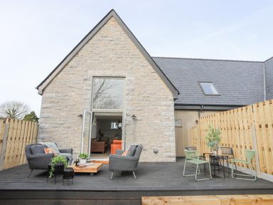 An outdoor patio with gray and green chairs wooden table and a stone house with a glass door at Ysgol Fach Little School in Benllech