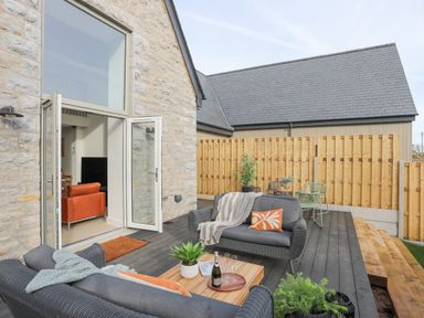 An outdoor patio with black wicker sofas, a wooden coffee table, plants, and a wooden fence at Ysgol Fach Little School in Benllech