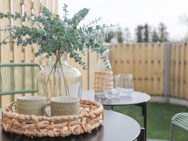 A patio with two tables holding a glass vase with leaves and cups with a wooden fence in the background at Ysgol Fach Little School in Benllech