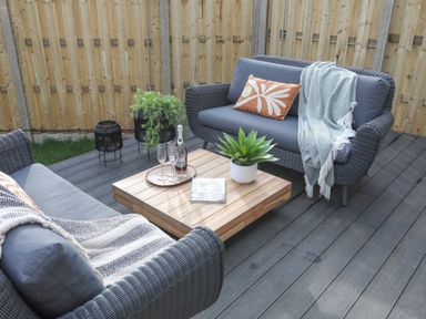 An outdoor seating area with two grey wicker sofas a wooden coffee table plants and a wooden fence at Ysgol Fach Little School in Benllech