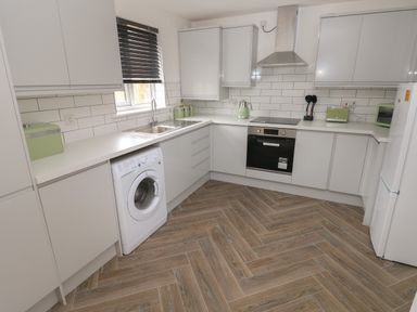A kitchen with white cabinets a washing machine an oven a sink window and wooden floor at 39 Mariners Quay in Port Talbot