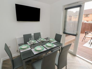 A dining room with six chairs around a glass table set with plates and wine glasses and a wall mounted TV at 39 Mariners Quay in Port Talbot