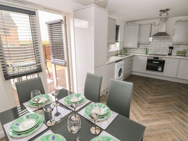 A kitchen with white cabinets a washing machine and an oven next to a dining table set with plates and wine glasses at 39 Mariners Quay in Port Talbot