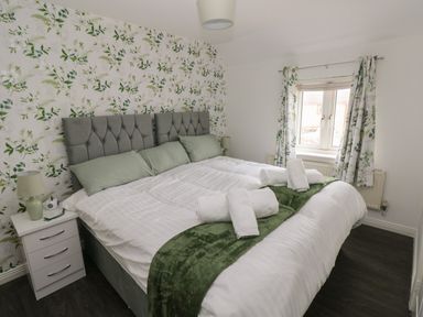 A bedroom with a large bed pillows bedside tables lamps and a window with curtains at 39 Mariners Quay in Port Talbot