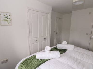 A bedroom with a bed with rolled white towels on a green runner and white doors on the wall at 39 Mariners Quay in Port Talbot