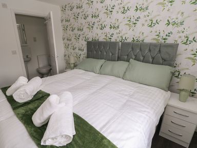 A bedroom with a double bed green pillows and rolled white towels beside a door leading to a bathroom at 39 Mariners Quay in Port Talbot