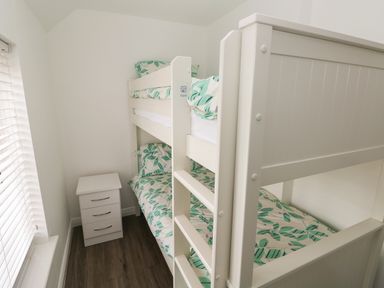 A bedroom with a white bunk bed with patterned bedding and a white bedside table by a window at 39 Mariners Quay in Port Talbot