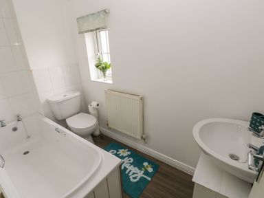 A bathroom with a bathtub toilet sink window and a blue mat on the floor at 39 Mariners Quay in Port Talbot