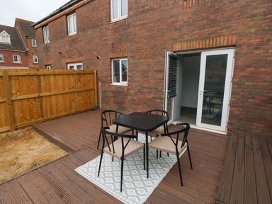An outdoor patio area with a table and four chairs on a wooden deck with a door leading inside at 39 Mariners Quay Port Talbot