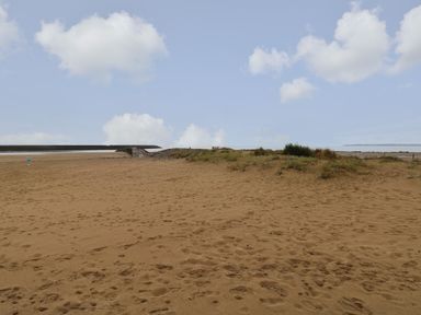 A sandy beach with grass patches and a stone pier under a partly cloudy sky at 39 Mariners Quay in Port Talbot