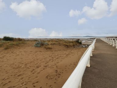 A sandy beach area with some vegetation next to a paved walkway with white railings at 39 Mariners Quay in Port Talbot