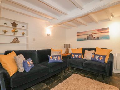 A living room with two dark sofas with various cushions a side table with a lamp and wall art at Blacksmiths Cottage in Crantock