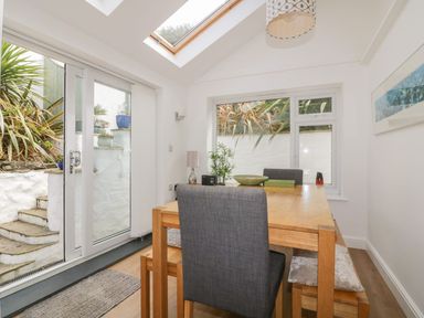 A dining area with wooden table and grey chairs near glass door and window at Blacksmiths Cottage in Crantock