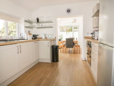 A kitchen with white cabinets wooden countertops and a dining table with chairs at Blacksmiths Cottage in Crantock