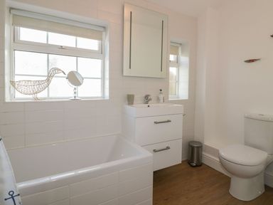 A bathroom with a bathtub sink with cabinet mirror toilet and windows at Blacksmiths Cottage Crantock