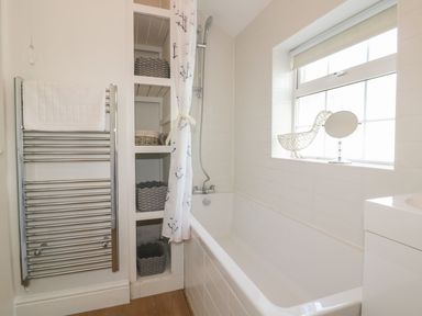 A bathroom with a bathtub shower white tiled walls shelving with baskets towel rail and a window with a decorative duck at Blacksmiths Cottage Crantock