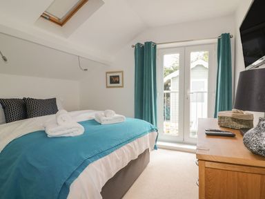 A bedroom with a bed with folded towels, teal curtains, skylight window, dresser with lamp and remote at Blacksmiths Cottage in Crantock