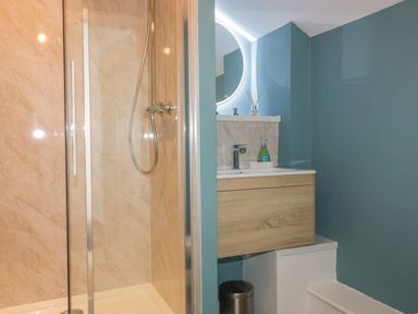 A bathroom with a glass shower enclosure and a wooden vanity unit with a sink at Blacksmiths Cottage in Crantock