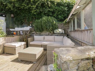 An outdoor seating area with a wicker sofa and table on a wooden deck at Blacksmiths Cottage in Crantock