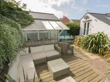An outdoor patio area with cushioned wicker seating and a glass top table surrounded by plants at Blacksmiths Cottage in Crantock