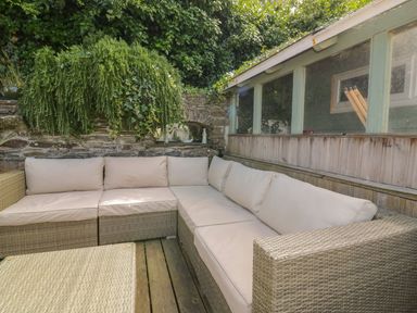 An outdoor seating area with a wicker corner sofa and a wicker table on a wooden deck at Blacksmiths Cottage in Crantock