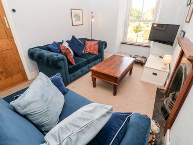 A living room with blue sofas, a wooden coffee table, a wall-mounted TV, and a fireplace at Pentira in Kuggar