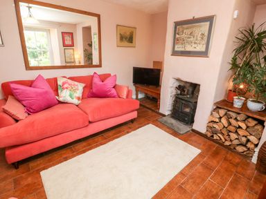 A living room with a red sofa and pink cushions near a fireplace and a stack of firewood at Pentira in Kuggar