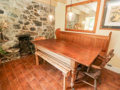 A dining area with a wooden table a bench a chair and a stone wall with a small fireplace at Pentira in Kuggar