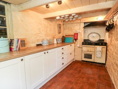 A kitchen with white cabinets wooden countertop stove hanging mugs and cooking pots at Pentira in Kuggar