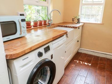 A kitchen counter with a microwave washing machine dishwasher sink and potted plants on the window sill at Pentira in Kuggar