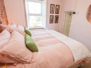 A bedroom with a bed with pink bedding and green pillows a window with shutters and framed artwork on the wall at Pentira in Kuggar